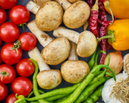Legumes variados como tomates, cogumelos, pimentos, cebola e alho vistos de cima.