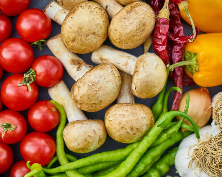 Legumes variados como tomates, cogumelos, pimentos, cebola e alho vistos de cima.