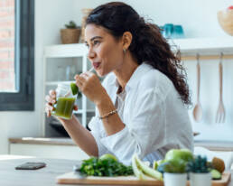Mulher a beber um sumo verde com vegetais frescos na cozinha.